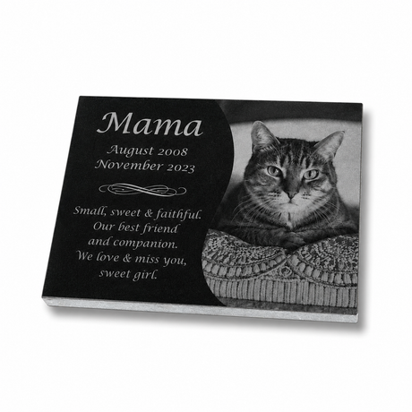 A rectangular memorial plaque shown at an angle on a white background. The left side is black with white text reading 'Mama' and dates and "Small, sweet & faithful. Our best friend and companion. We love & miss you, sweet girl", while the right side shows a grayscale photo of a cat resting on a patterned cushion.