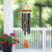 A hanging black wind chime with an orange top and wooden clapper with wording: Mothers hold their children's hands for a little while but their hearts forever, hangs with a blurred outdoor porch setting in the background.