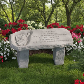 A gray stone tablet featuring an angel design on the left and an engraved poem that begins with "Those we love don't go away, they walk beside us every day. Unseen, unheard, but always near, so loved, so missed, so very dear.  Garden setting with colorful floral surroundings.