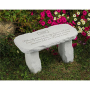 A gray stone bench in a garden surrounded by colorful flowers, featuring an engraved inscription that reads, "Although your smile is gone forever, and your hand I cannot touch, I still have so many memories of the one I loved so much".